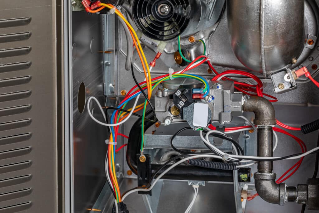 An interior view of a mechanical device showing various wires in multiple colors connected to components, including a black fan and a gray box. Metal pipes and a cylindrical part are also visible against a metallic background.